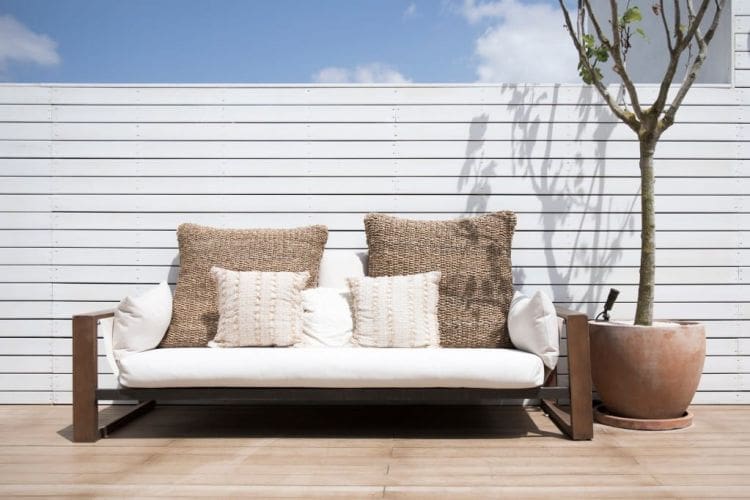 view-of-a-modern-simplistic-white-outdoor-sofa-on-a-deck-of-a-house-with-a-lone-tree-in-a-ceramic-pot_t20_6l040N